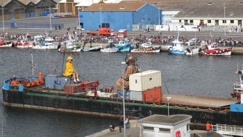 La petite géante est une marionnette, et son oncle le géant est revêtu d'une combinaison de scaphandrier. Le scaphandrier apporte avec lui la malle postale du Titanic, qu'il a extraite de l'Océan pour en délivrer le contenu de 90.000 lettres de passagers fictifs du Titanic, sont ainsi distribuées à coup de canon aux spectateurs.